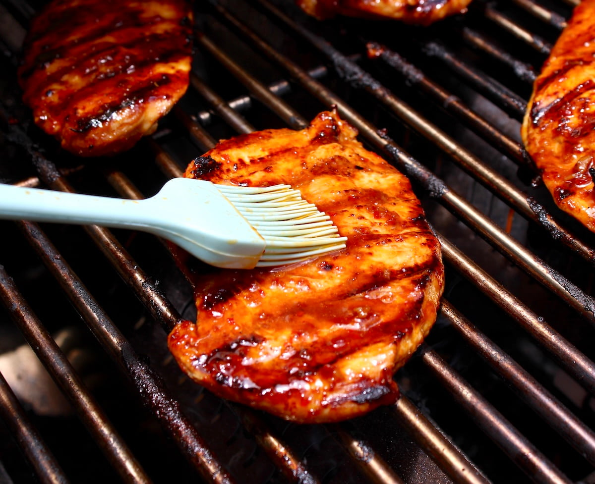 brushing asian marinade over chicken on grill