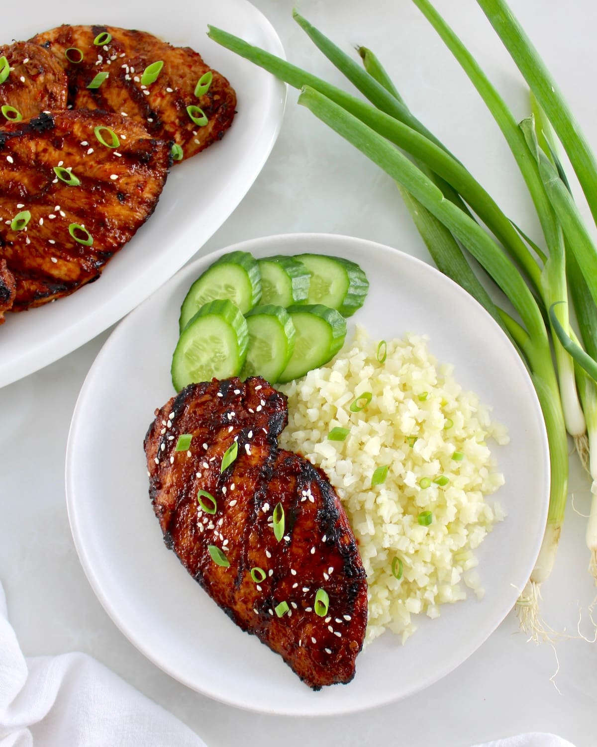 Grilled Asian Chicken on white plate with cauliflower rice and sliced cucumbers