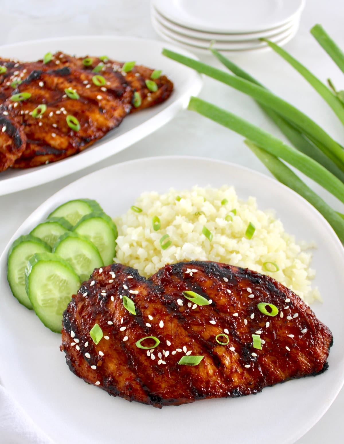 Grilled Asian Chicken on white plate with cauliflower rice and sliced cucumbers