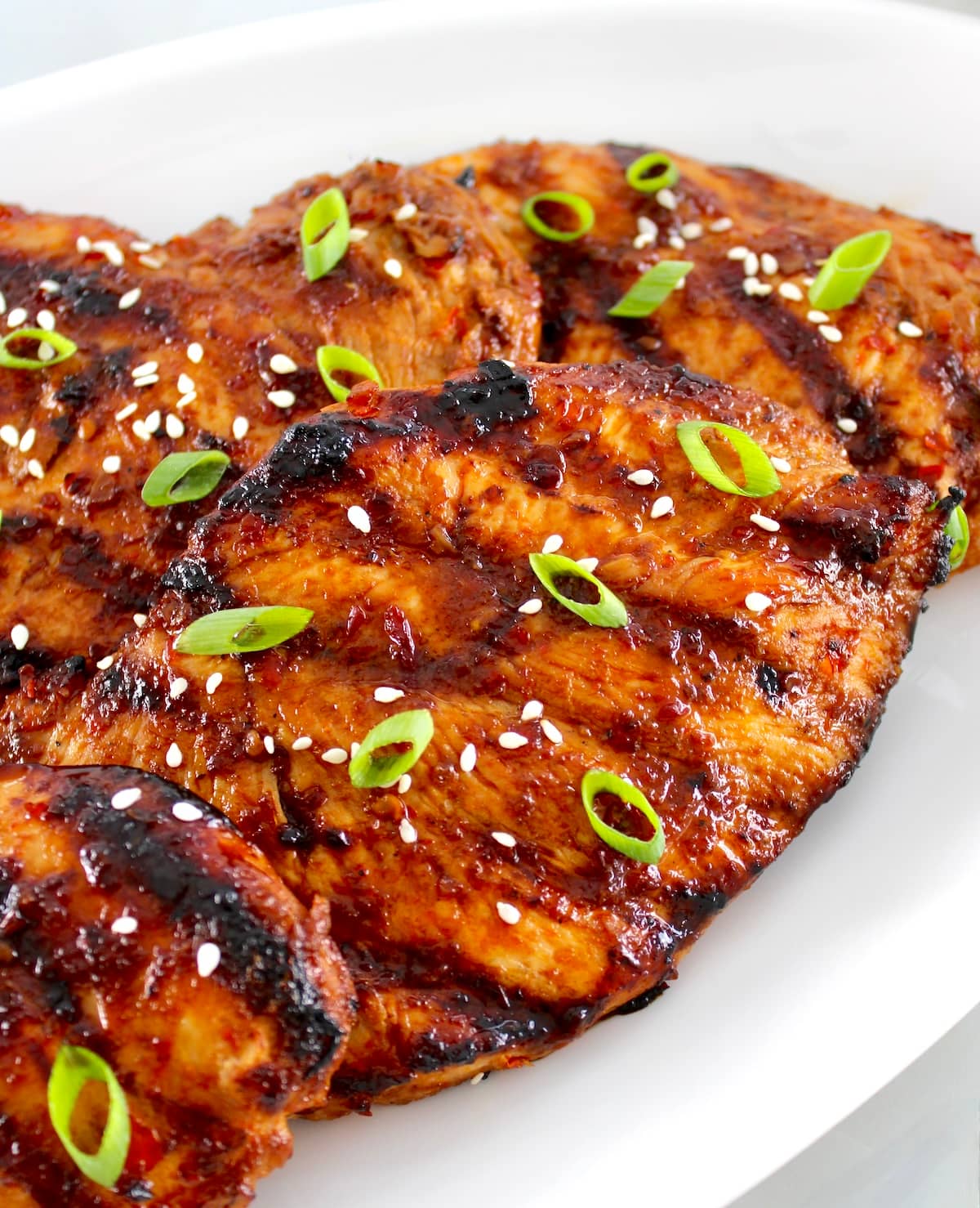 closeup of Grilled Asian Chicken on white plate with scallions on top