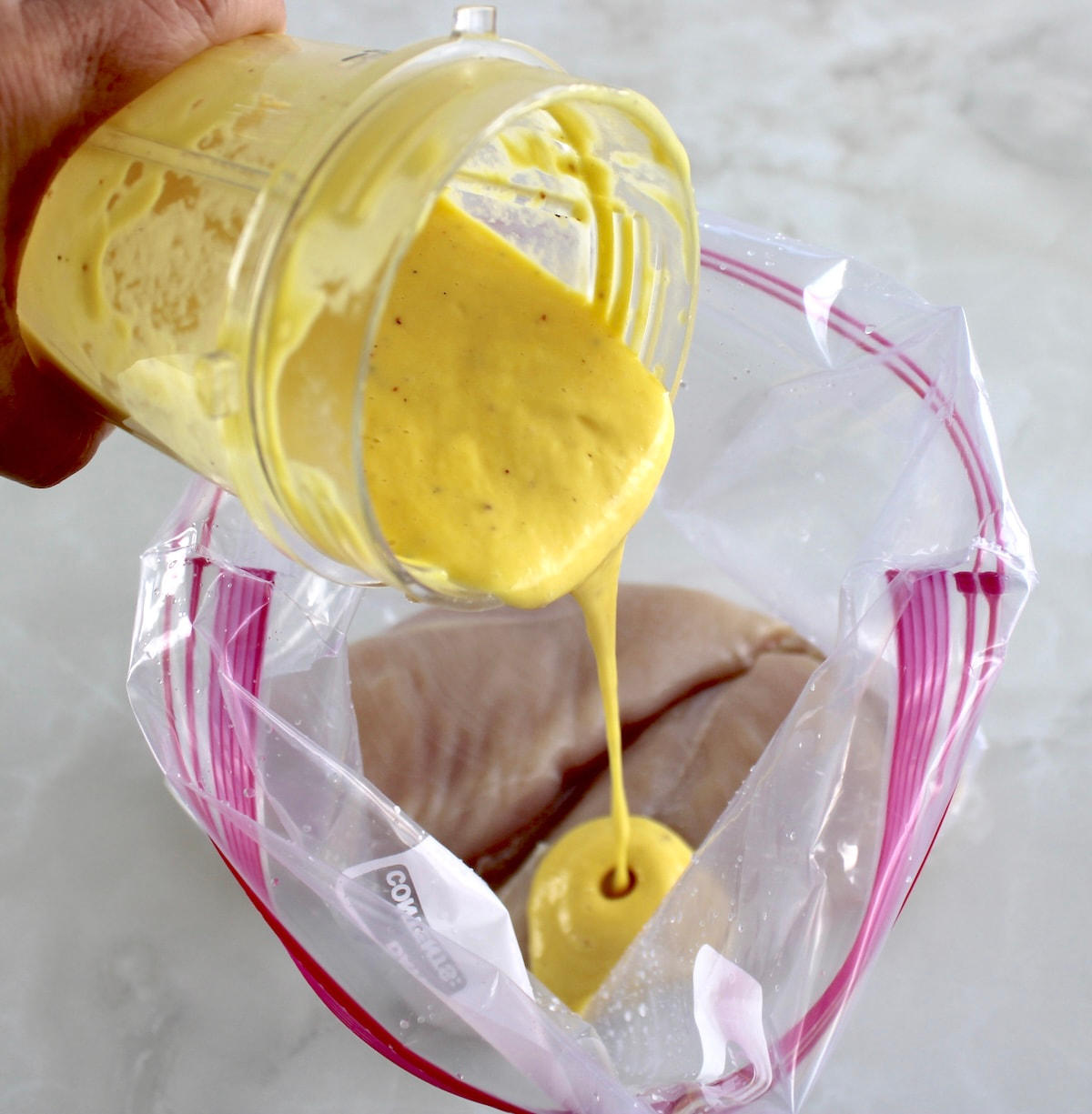mango dressing being poured over raw chicken in food storage bag