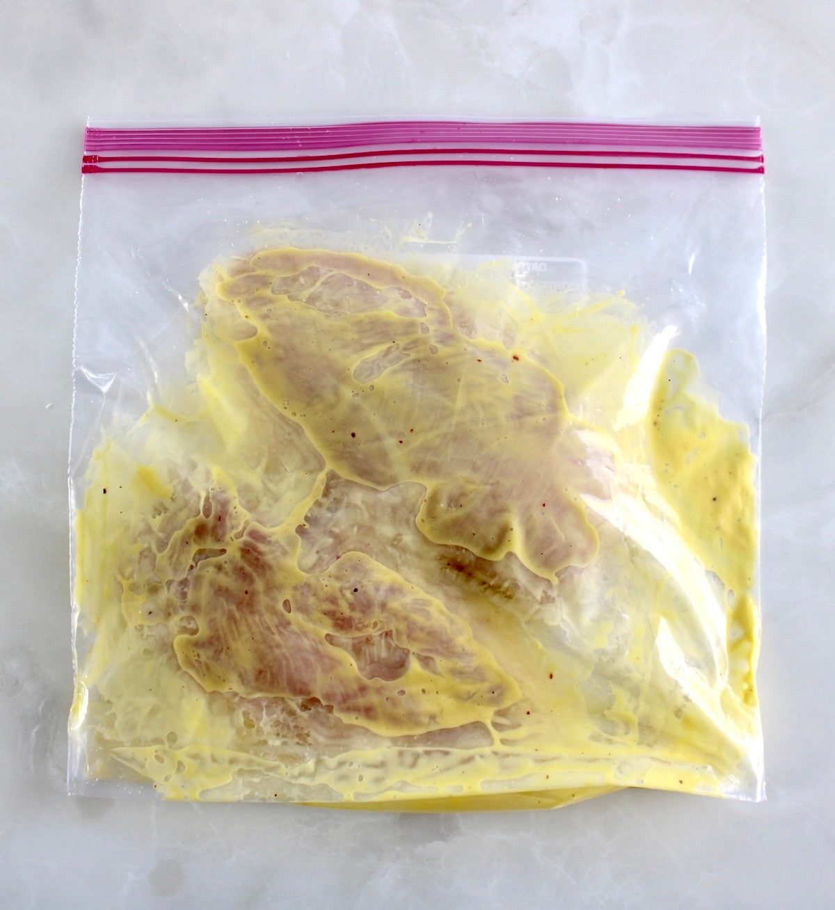 raw chicken marinating in mango dressing in food storage bag