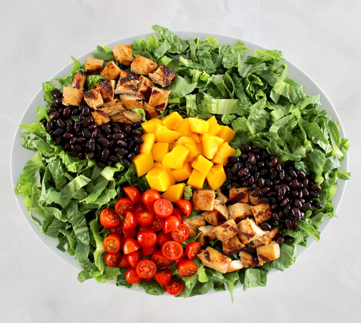 shredded lettuce with diced chicken, mango tomatoes and black beans on oval platter