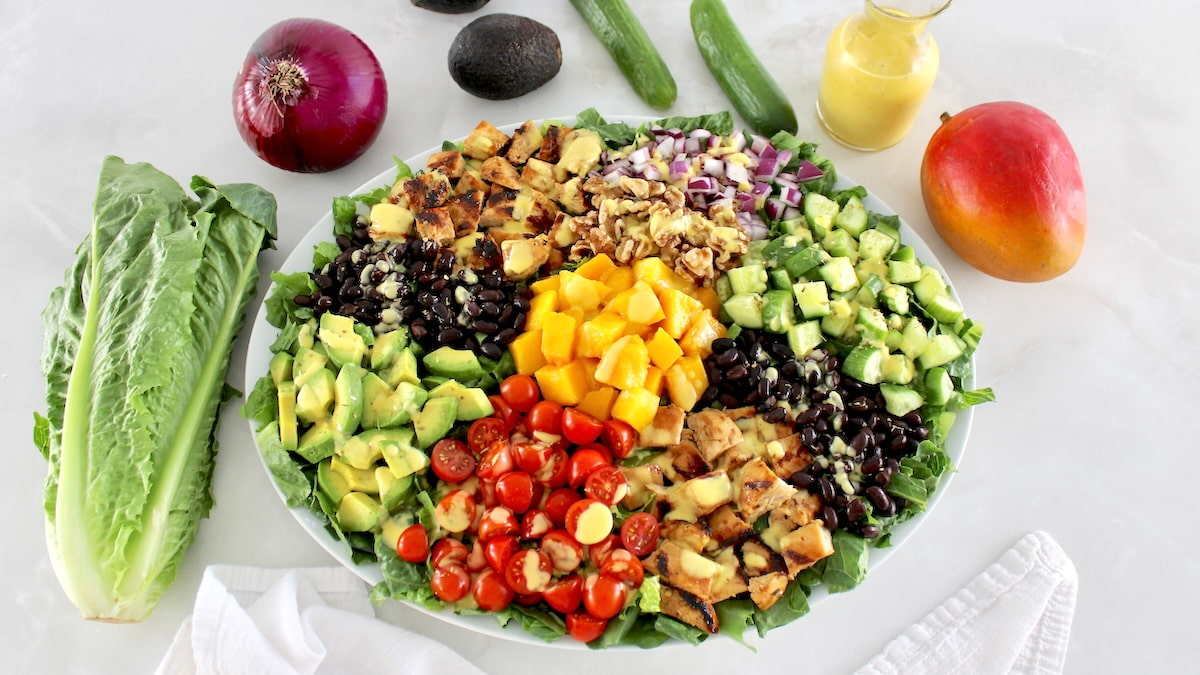 overhead view of Chopped Chicken Mango Salad on oval platter with fresh veggies in back