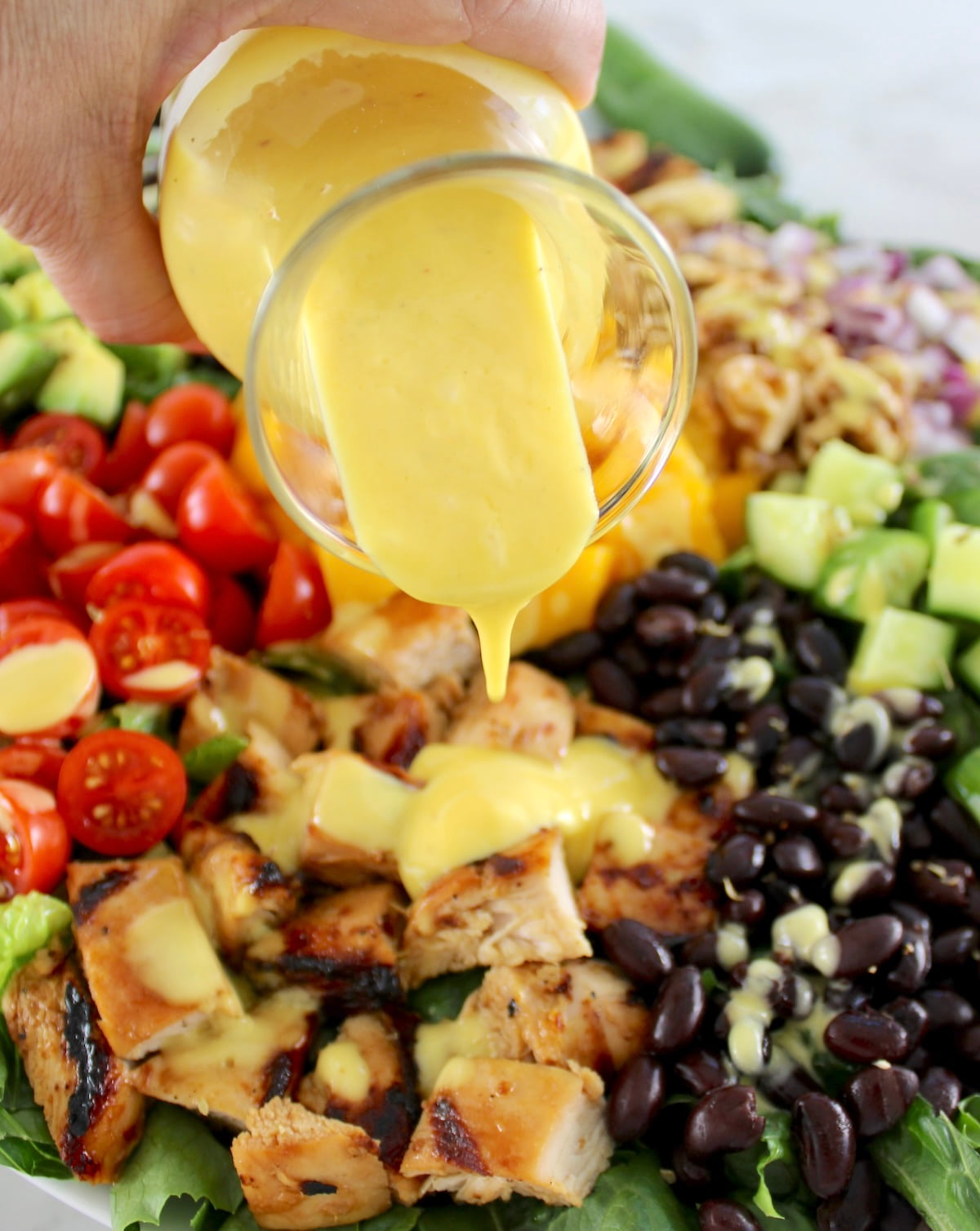 mango dressing being poured over Chopped Chicken Mango Salad