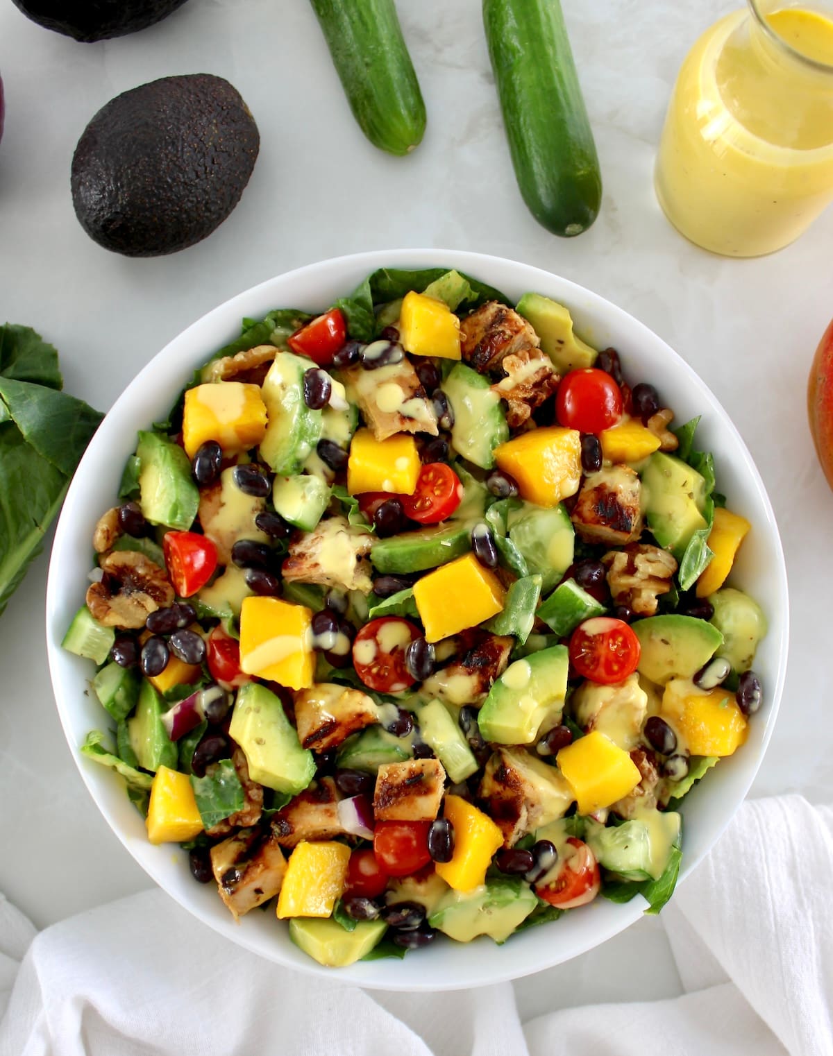 overhead view of Chopped Chicken Mango Salad in white bowl with fresh veggies in back