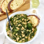 Escarole and Beans (Scarola e Fagioli) in white bowl with spoon and piece of bread on side