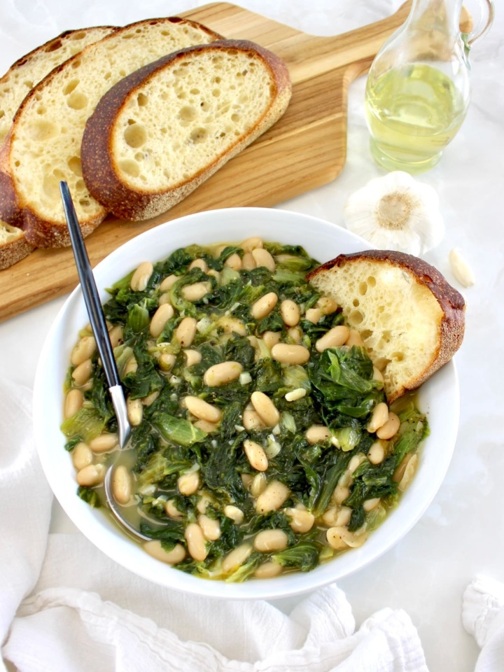 Escarole and Beans (Scarola e Fagioli) in white bowl with spoon and piece of bread on side