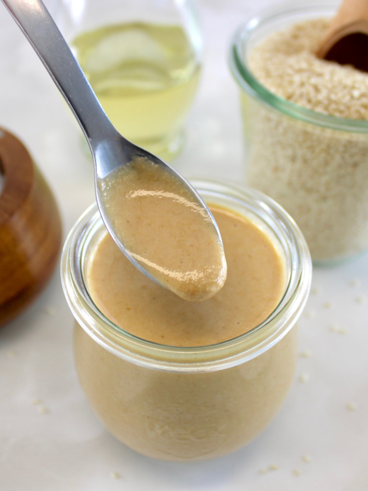 Homemade Tahini in spoon held over open glass jar