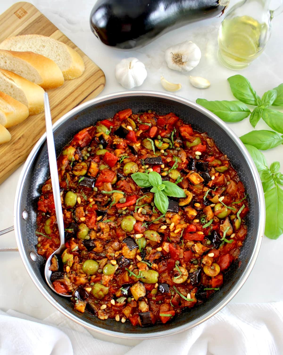 Eggplant Caponata in skillet with silver serving spoon on side and fresh basil garnish