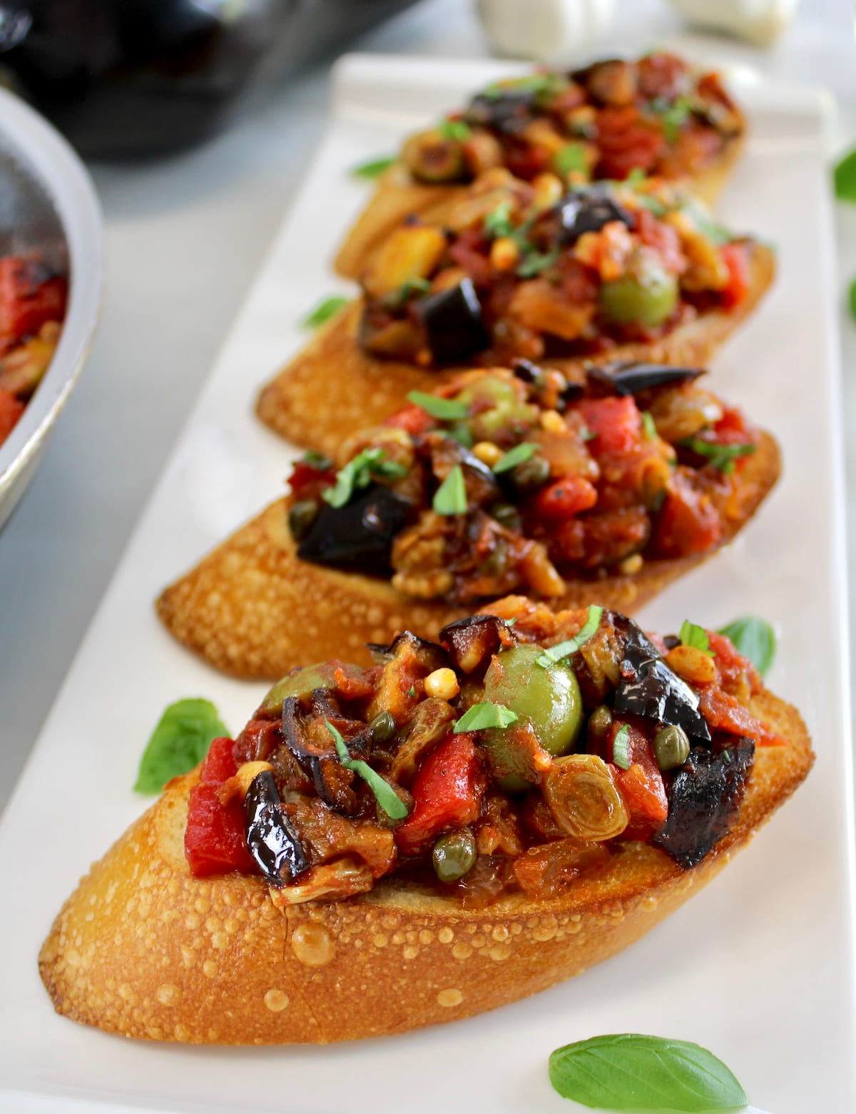 4 crostini with Eggplant Caponata on top on white platter