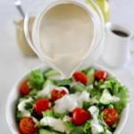 Maple Tahini Dressing in glass pitcher being poured over salad in white bowl