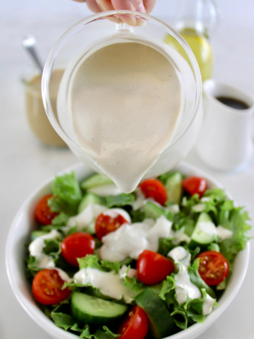 Maple Tahini Dressing in glass pitcher being poured over salad in white bowl