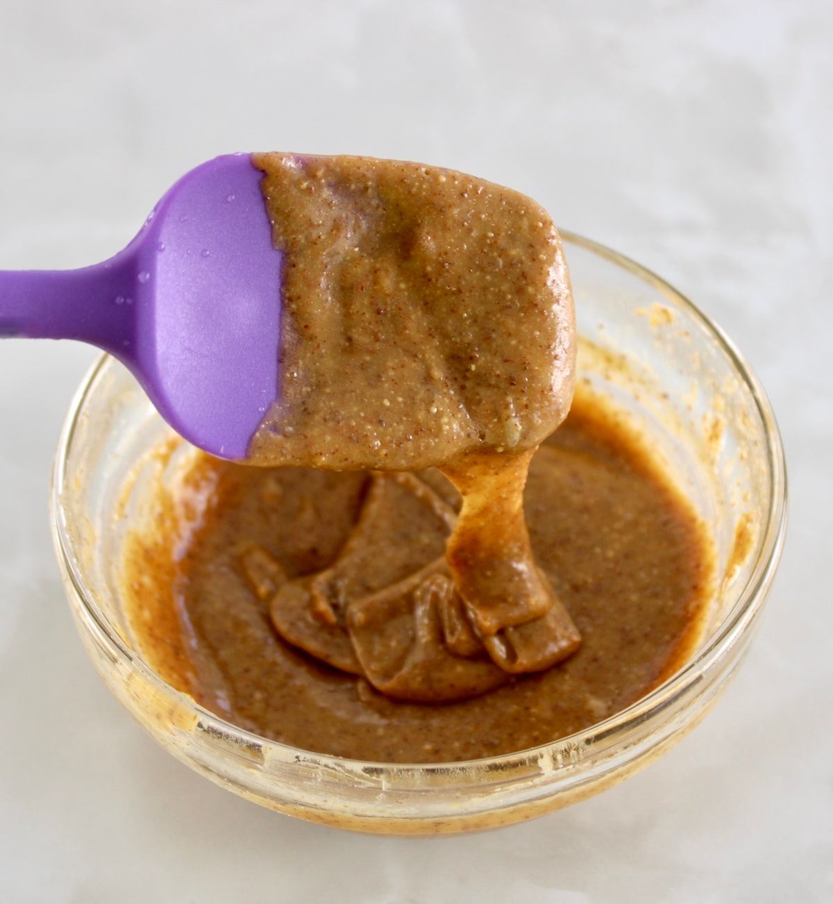 melted honey and almond butter dripping off purple spoon into glass bowl