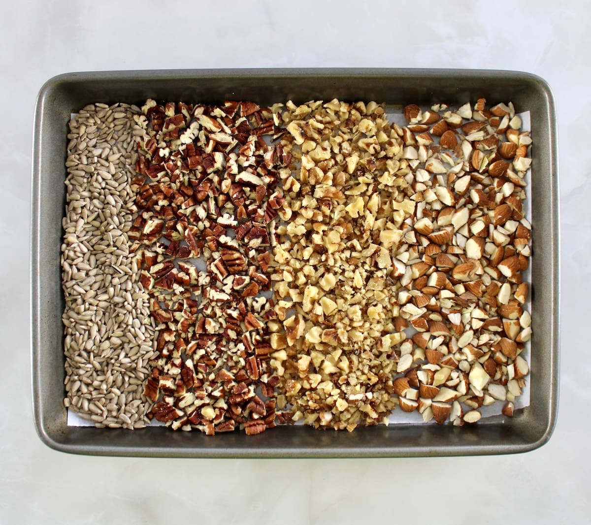 chopped nuts and sesame seeds on parchment lined baking sheet in rows