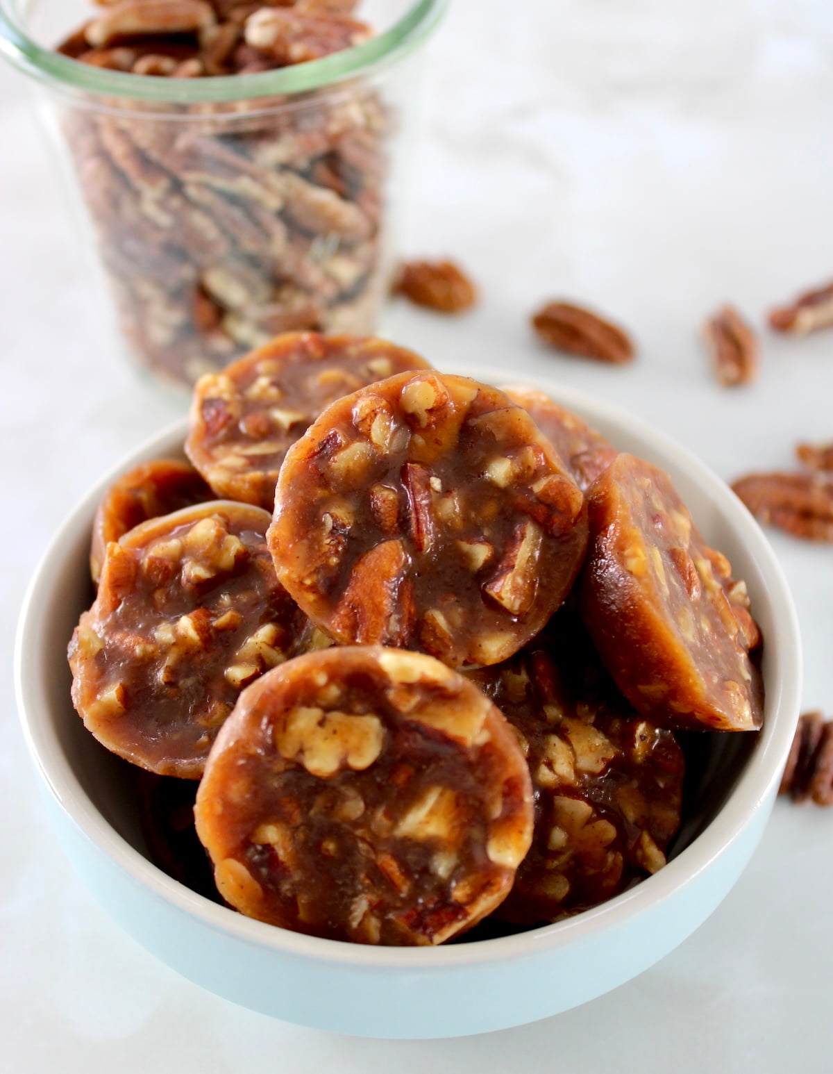 closeup of Pecan Caramel Clusters in blue bowl with pecans in back