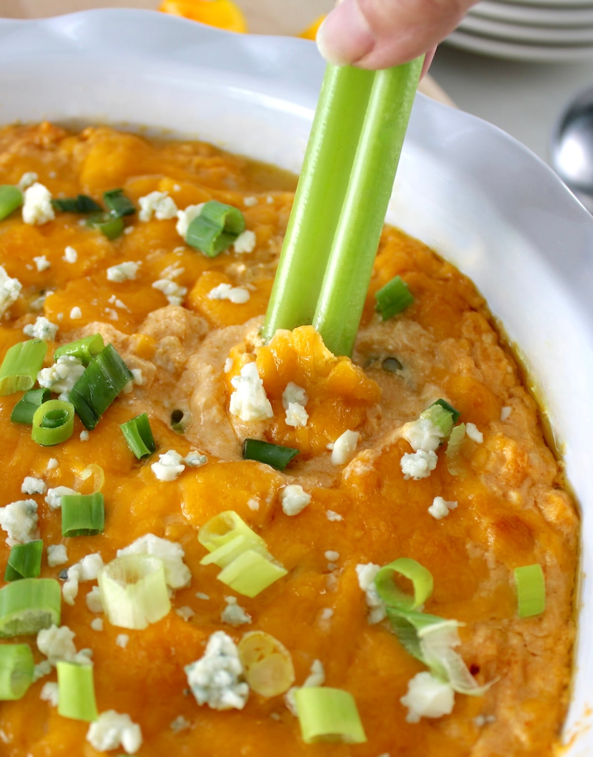 dipping celery stick into Cottage Cheese Buffalo Chicken Dip in white dish