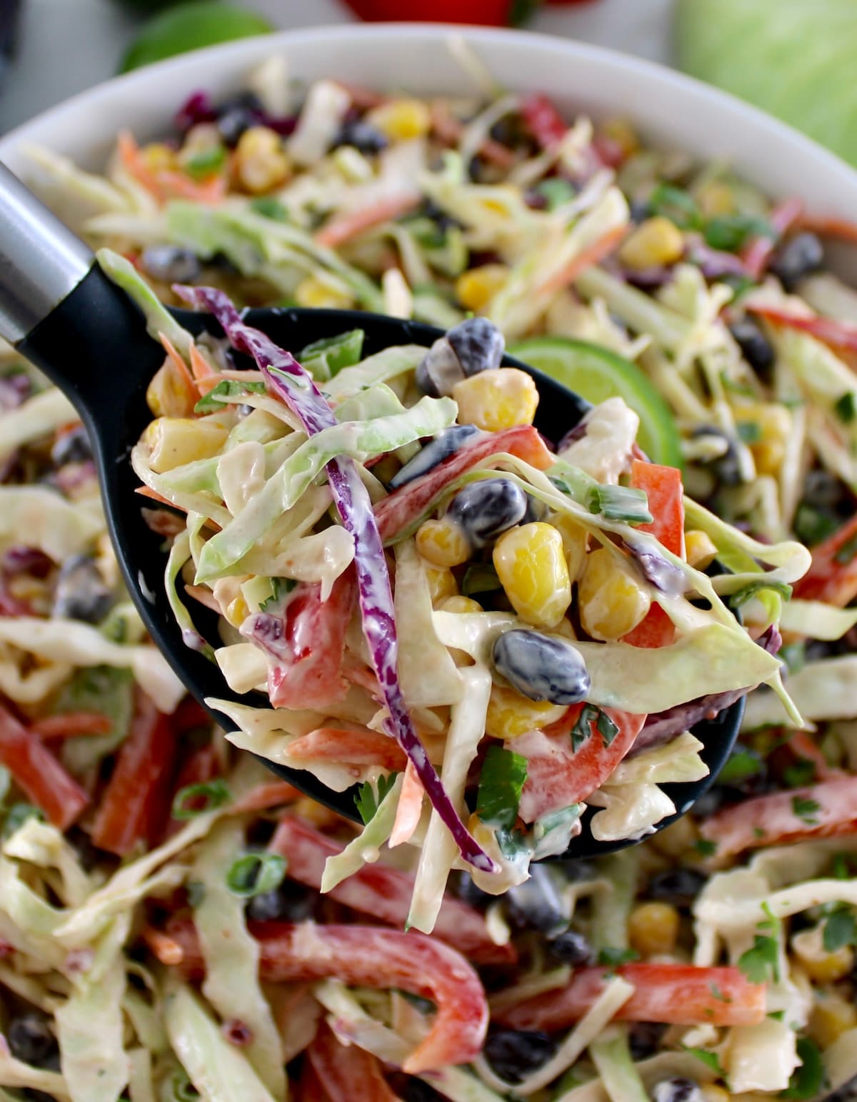 Cowboy Coleslaw in black serving spoon held up over white bowl