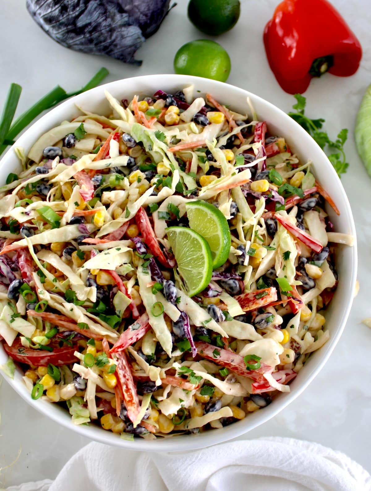 overhead view of Cowboy Coleslaw in white bowl with fresh veggies in back