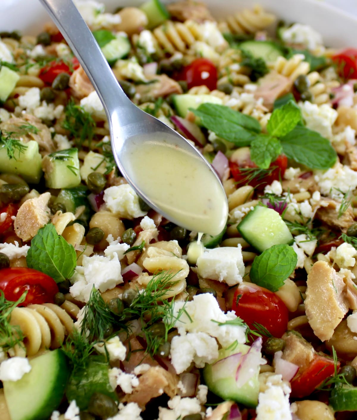 dressing being spooned over Chickpea Tuna Pasta Salad