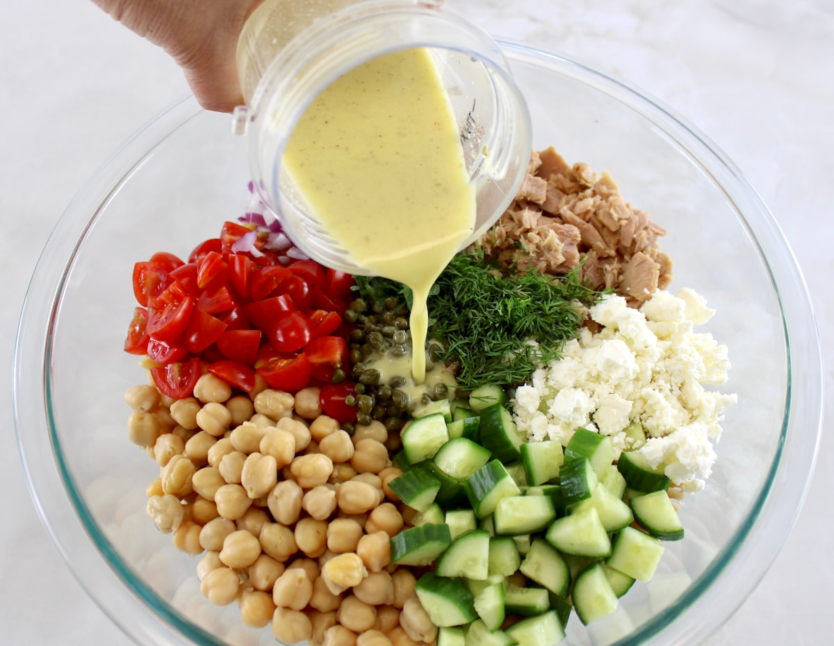 dressing being poured over Chickpea Tuna Pasta Salad ingredients in glass bowl unmixed