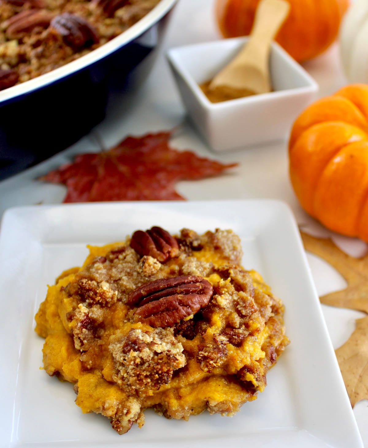 Pumpkin Casserole on white square dish with casserole and pumpkins in back